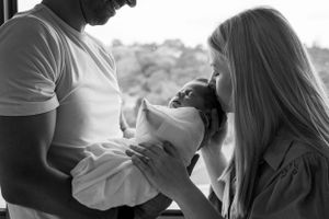Intimate black and white family moment with newborn wrapped in light swaddle.