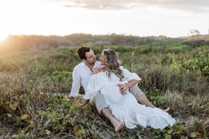 Couple relaxing on grassy hillside during sunset maternity session.