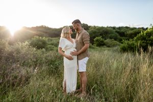 Couple embracing in golden sunlit field during maternity photoshoot.