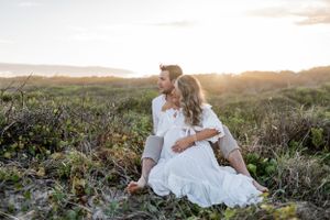 Couple sitting together on coastal dunes during golden hour photoshoot.