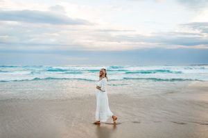 A person in a flowing white dress walks along the shoreline with turquoise waves crashing.