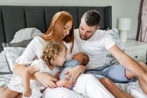 Family lounging together on bed with newborn baby in intimate lifestyle setting.