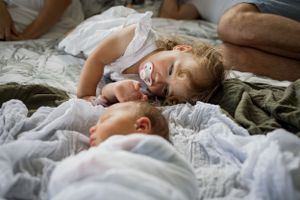 Toddler sleeping next to newborn sibling on white bedding.