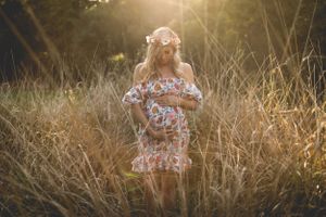 A maternity portrait in golden sunlight with floral off-shoulder dress amid tall grass.