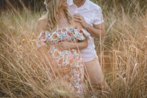 Romantic maternity photoshoot in tall grass field at sunset.