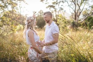 Couple embracing in sunlit field with tall grass during golden hour.