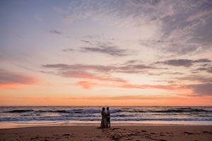 Beautiful sunset sky with layers of pink and orange clouds reflecting over a serene beach shoreline.