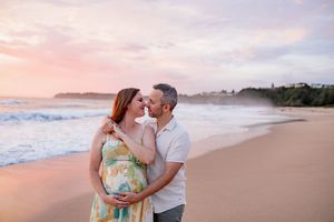 Two people share a romantic moment on a scenic beach at sunset with gentle waves and pink sky in the background.