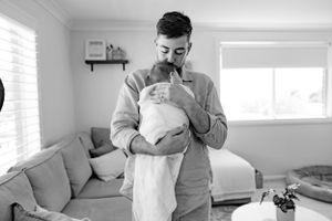 A monochrome image showing a gentle moment with a newborn wrapped in white.