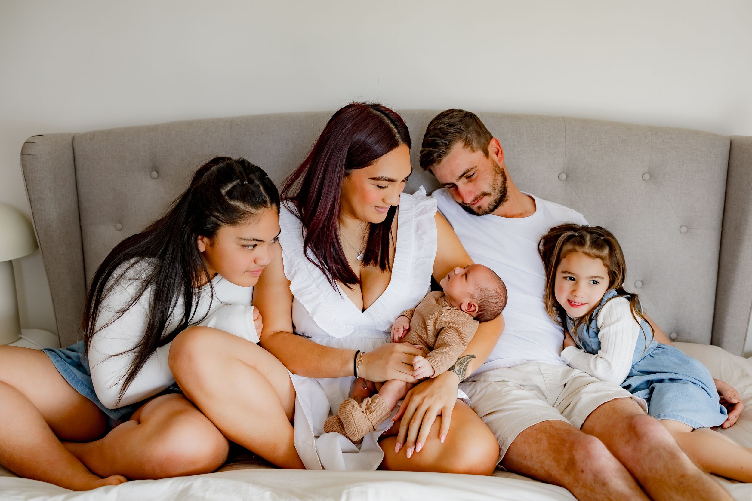 Intimate family portrait on bed showing newborn with siblings and parents.