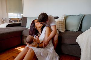 Intimate moment shared between couple with newborn on gray couch.