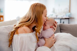 A tender moment captured between mother and newborn baby in white clothing on a couch.