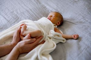 A resting baby swaddled in a soft cream-colored blanket lies peacefully on a gray surface.