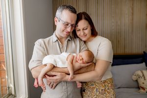 A baby rests peacefully while surrounded by family members on a cozy couch in a warmly lit room.