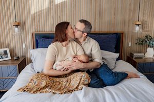 A couple sharing an intimate kiss while sitting on a bed with rustic wooden walls and decor in the background.