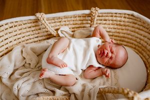 Sleeping newborn baby wrapped in white swaddle rests peacefully in a woven basket bassinet.