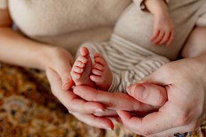 Adult hands gently holding tiny baby feet on a patterned rug in warm natural light.