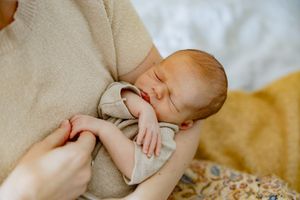 Gentle hands caress the delicate feet of an infant while lying on soft tan bedding.