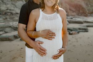 Close-up maternity photo showing loving embrace on a rocky beach at golden hour.
