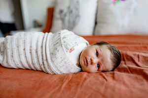Newborn baby wrapped in a striped swaddle blanket resting on orange bedding.