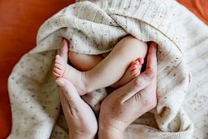 Tiny baby feet being gently held in adult hands with a soft polka dot blanket on orange background.