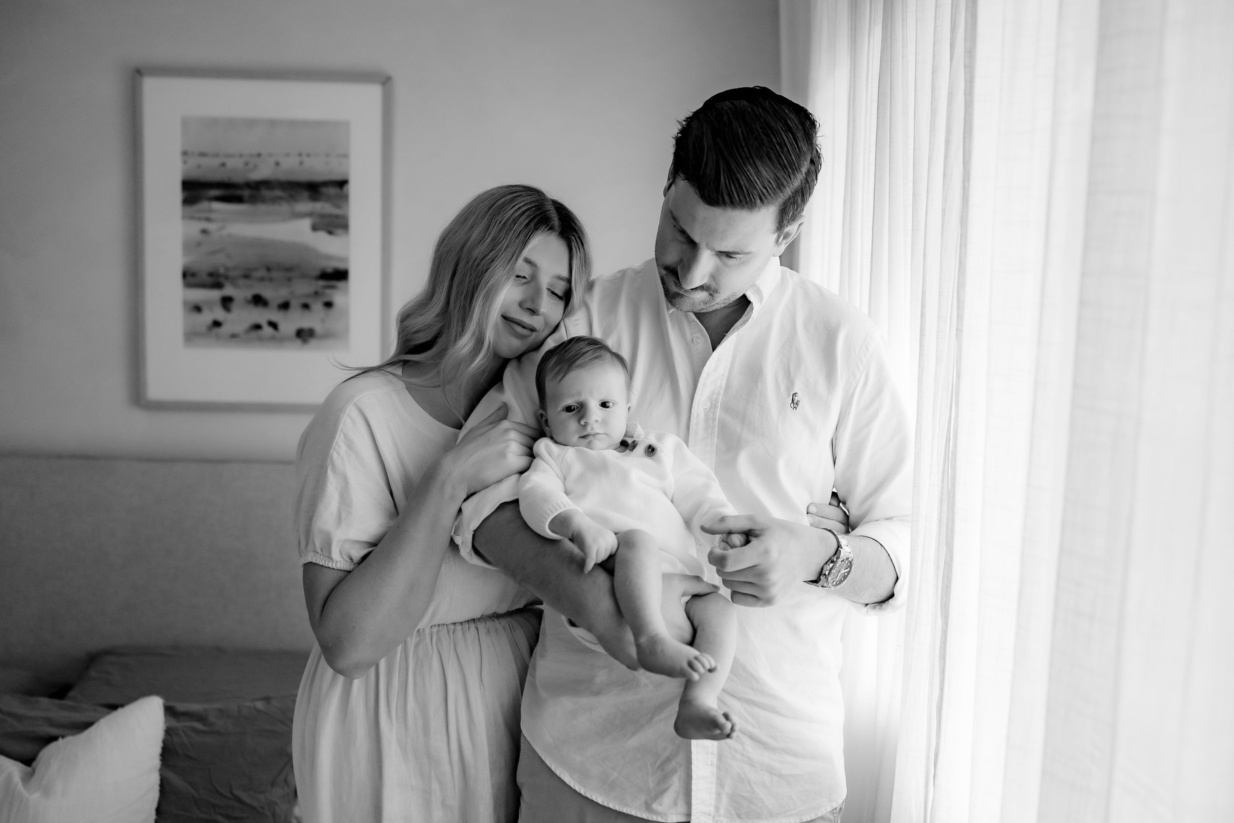 A black and white portrait of a family sharing a tender moment by a sunlit window.