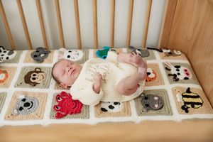 A resting baby lying on a patchwork quilt with embroidered animals and flowers creates a cute nursery scene.