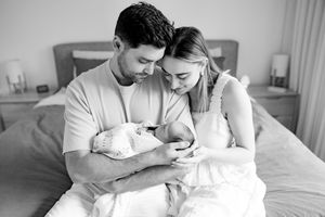 New parents share intimate moments caring for their newborn baby at home in a relaxed bedroom setting.