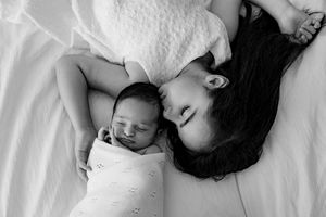 Black and white photograph of a sleeping baby lying on white bedding with soft, gentle lighting.