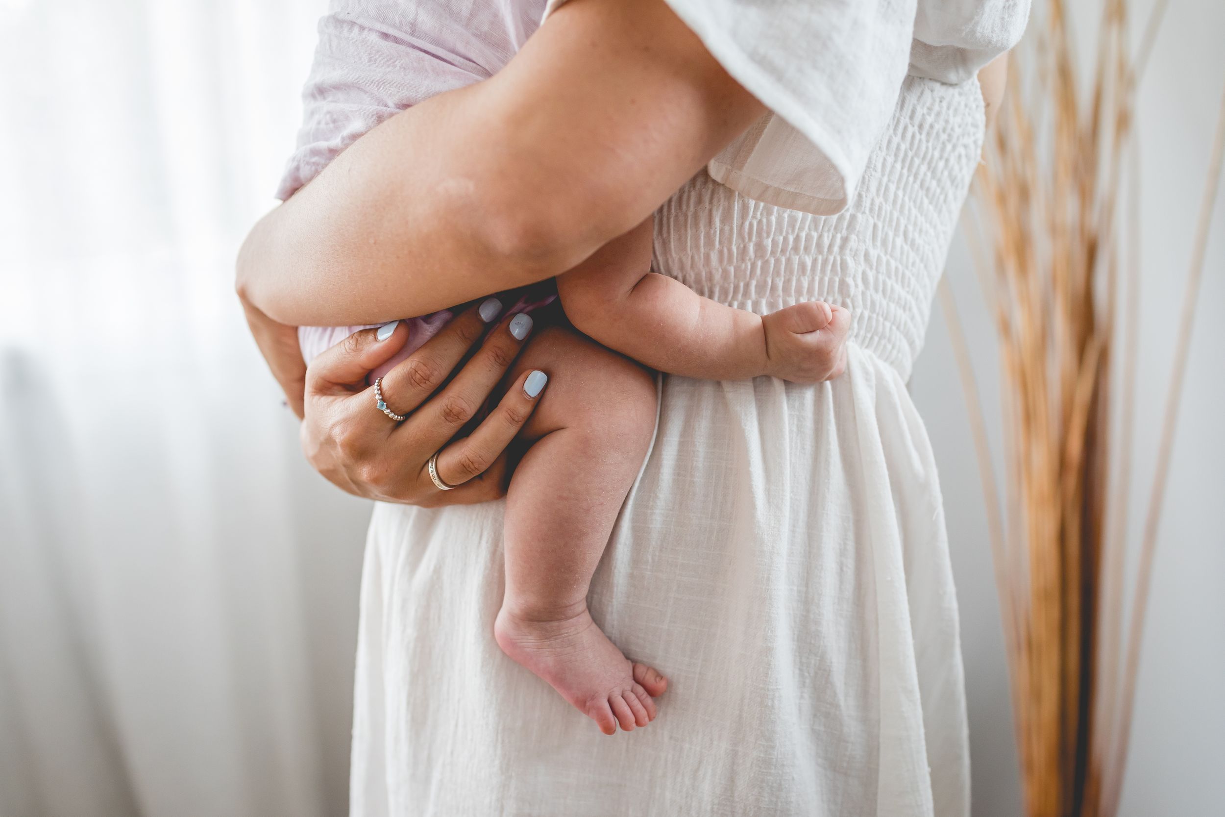 Close-up view of tiny baby feet being held against a white dress.