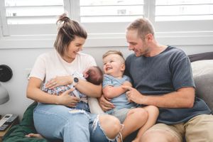 Family relaxing together on a grey couch with their young children.