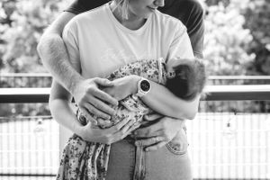 Black and white image capturing tender moment with infant being held outdoors.