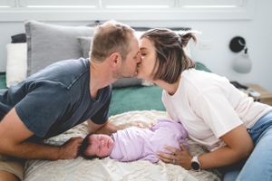 Parents sharing a tender moment with their newborn on a bed.