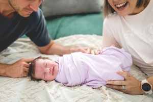 A baby in pink sleepwear rests peacefully between parents on a patterned blanket.