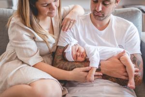 Tender moment with newborn baby resting on grey couch.
