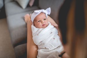 Baby wearing white bow headband and wrap looking at camera.