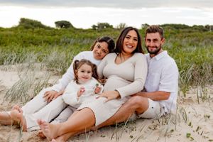 Family maternity photo on beach with everyone wearing coordinated white and neutral outfits.