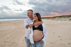 Maternity photo of couple on beach during sunset wearing casual attire.
