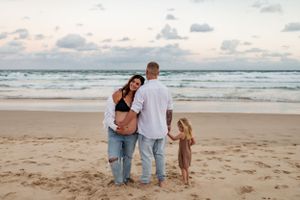 Family standing together watching ocean waves at sunset on beach.