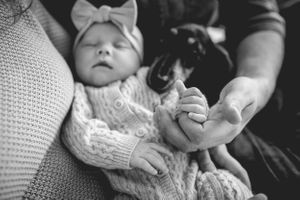 A black and white photo of a sleeping newborn with bow headband next to a small black dog.