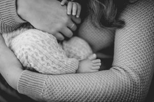 Close-up black and white image of a baby wearing a knitted sweater being held tenderly.