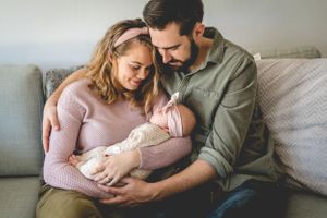 A tender moment between parents and their newborn baby on a grey couch in natural light.