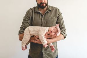 Baby in knit outfit being cradled in parent's arms.