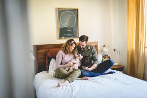 A family moment with a newborn baby on a bed under a wall clock.
