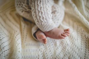 Tiny baby feet wearing a knit sweater resting on a white textured blanket.