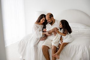 Family enjoying tender morning moments together on white bedding in natural window light.