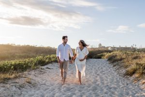Couple walking together on sandy beach path during golden hour sunset.