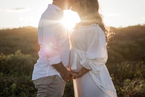 Romantic silhouette of couple embracing during golden hour with sun flare between them.