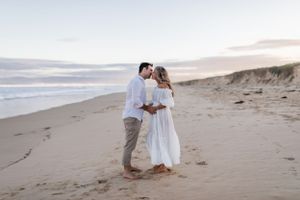 A romantic couple embraces on a sandy beach during sunset.