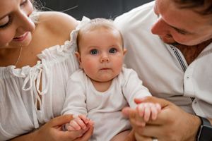 An intimate family moment captured with a baby between parents on white bedding.